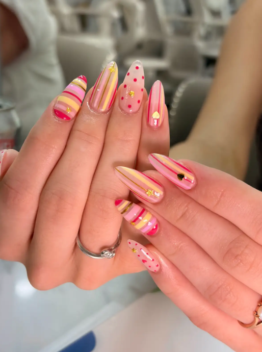 Pink and gold striped nails with polka dots, gold star and heart charms